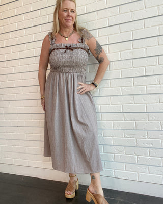 Brown gingham midi dress with smocked bodice, shoulder straps, and velvet trim accents styled for a feminine vintage-inspired outfit.
