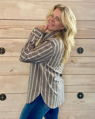 Woman wearing a striped shirt and jeans against a wooden wall.