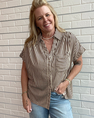 Woman wearing a striped shirt and jeans standing against a light brick wall.