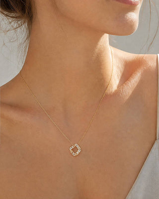 A close-up of a model's neck and upper chest wearing a delicate gold chain necklace with a small square pendant set with clear stones.