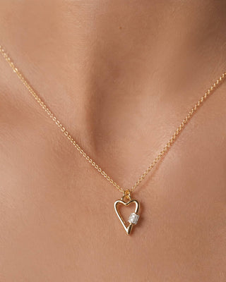 A delicate gold chain necklace with an open heart pendant featuring a small clear gemstone, shown worn on a model's neck.