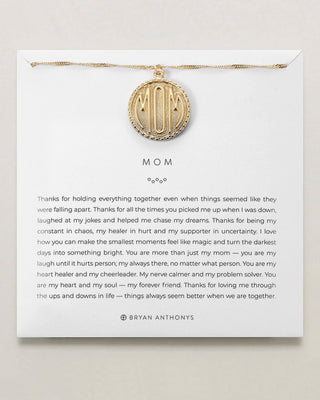 Gold necklace with a 'Mom' pendant on a white card with text.