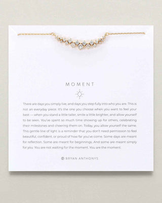 A delicate gold chain necklace with a curved row of small clear rhinestone-like stones, displayed on a white printed card with inspirational text. The card is branded BRYAN ANTHONYS.