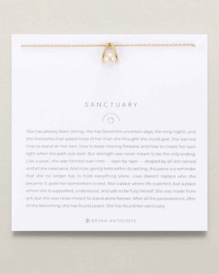 A white card with a gold-toned pendant necklace displayed at the top and a long block of inspirational text titled 'SANCTUARY' by Bryan Anthonyons below, photographed against a light neutral background.