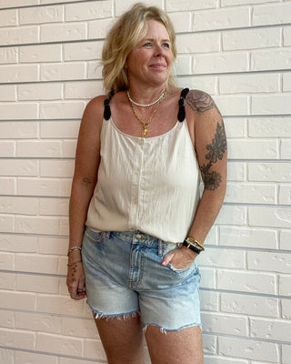 Women's cream sleeveless button-front top with faux leather buckle straps, lightweight woven fabric, and a relaxed fit.