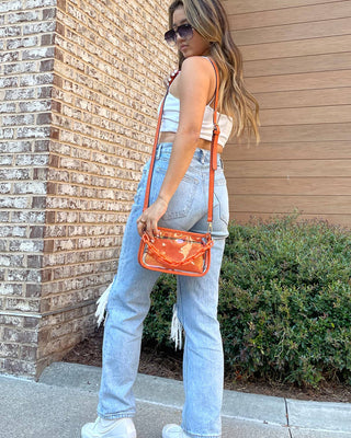 Woman holding an orange handbag against a brick wall