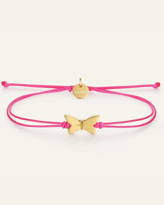 A pink adjustable cord bracelet with a gold butterfly charm and a small round gold disc engraved with the brand name 'mantra', shown on a light cream background.