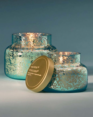Two turquoise glass candles with gold lids on a gray background