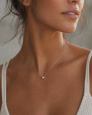 Close-up of a woman wearing a delicate gold necklace with a small pendant.