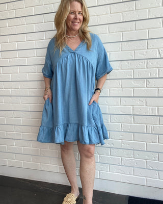 Woman wearing a blue dress standing against a white brick wall.