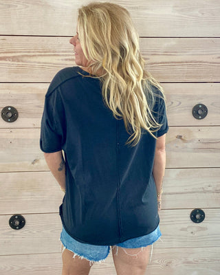 Person wearing a navy shirt and denim shorts standing against a wooden wall.