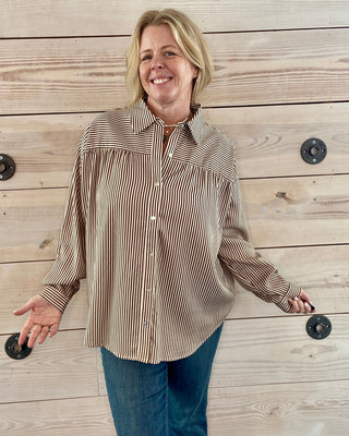 Woman wearing a striped shirt and jeans standing against a wooden wall.