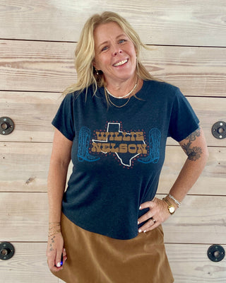 Person wearing a blue t-shirt with 'Willie Nelson' design against a wooden wall.