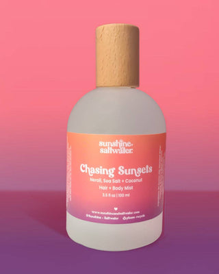 Bottle of 'Chasing Sunsets' hair and body mist with a cork cap on a pink gradient background.