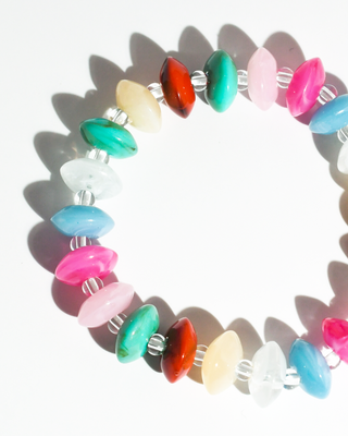 A beaded stretch bracelet made of polished, elongated gemstone-like beads in multiple colors including pink, blue, green, red, and white, separated by small silver spacer beads, shown on a white background with hard shadows.
