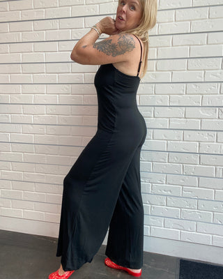 Women's black wide leg jersey jumpsuit with adjustable spaghetti straps, V-neckline, and a relaxed full-length silhouette.