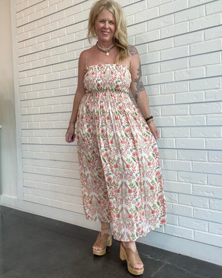 Woman wearing a floral dress standing against a white brick wall.