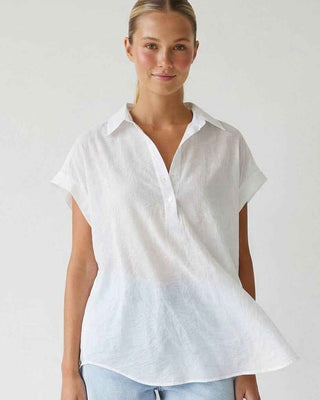 Woman wearing a white short-sleeve shirt and light blue shorts on a plain background