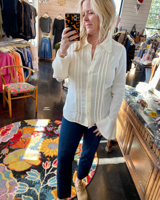 Woman taking a mirror selfie in a clothing store wearing a white blouse and blue jeans.