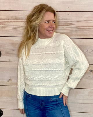 Woman wearing a white sweater and blue jeans standing against a wooden background