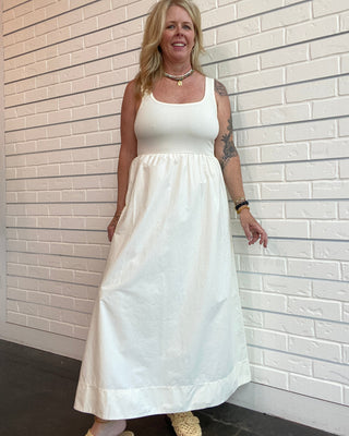 Woman wearing a white dress standing against a tiled wall.