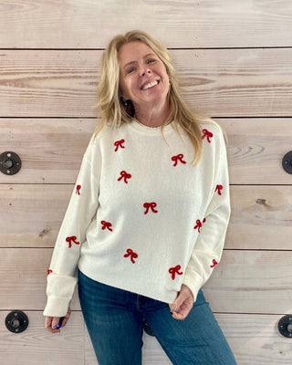 Woman wearing a white sweater with red bows against a wooden background