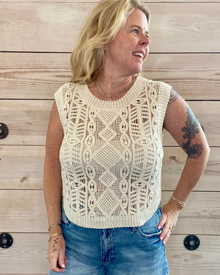 Woman wearing a beige lace top and denim shorts against a wooden background