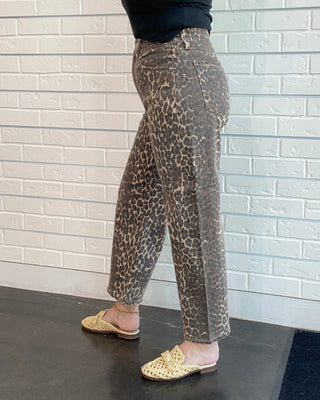 Woman wearing leopard print pants and a black top against a white brick wall.