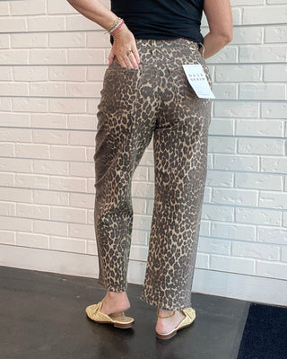 Person wearing leopard print pants and a black top against a white brick wall.