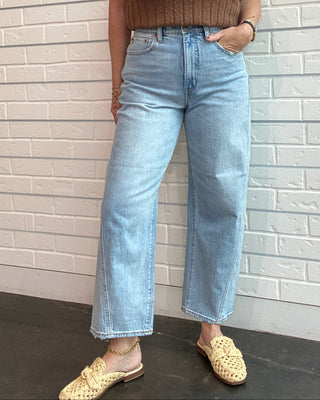 Person wearing a brown top and light blue jeans standing on a tiled floor.