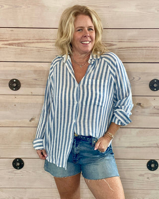 Woman wearing a blue and white striped shirt and denim shorts standing against a wooden wall.
