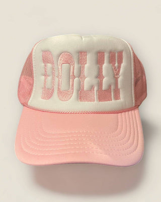A pink and white trucker hat with 'DOLLY' embroidered on the front, set against a light beige background.
