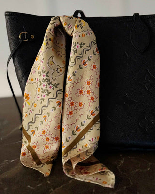 Black handbag with a floral scarf draped over it on a marble surface