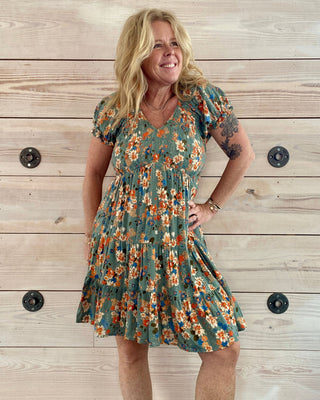Woman wearing a floral dress standing against a wooden wall.