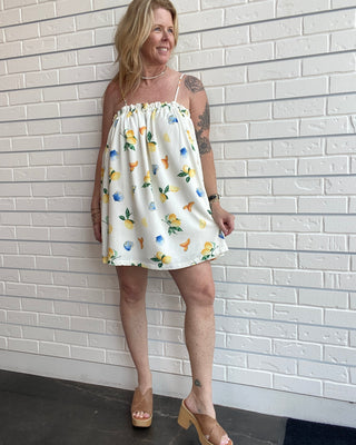 Woman wearing a floral dress against a white brick wall.
