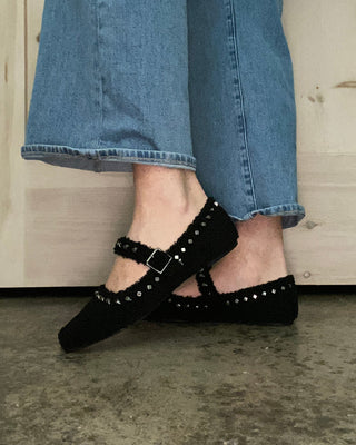 Person wearing blue jeans and black studded shoes on a wooden floor.