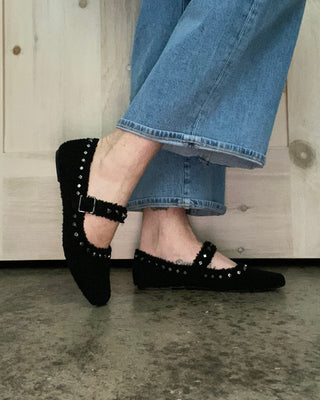 Person wearing black studded shoes and blue jeans on a wooden floor.