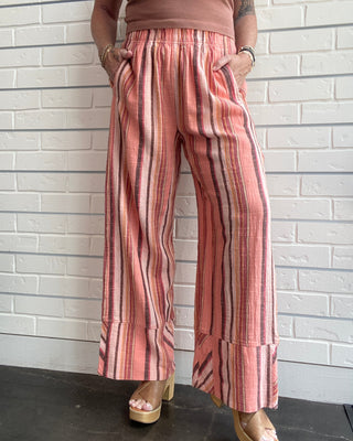 Person wearing pink striped pants and a brown top against a white brick wall.