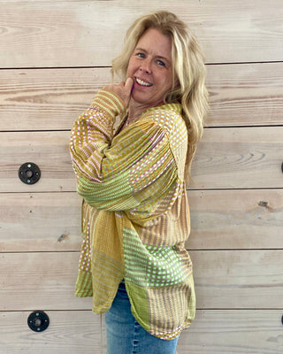 Woman wearing a patterned yellow shirt against a wooden wall.