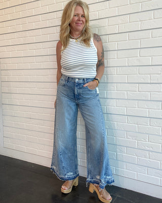 Woman wearing a striped top and wide-leg jeans against a white brick wall.