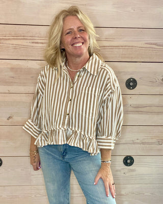 Woman wearing a striped shirt and jeans standing against a wooden wall.
