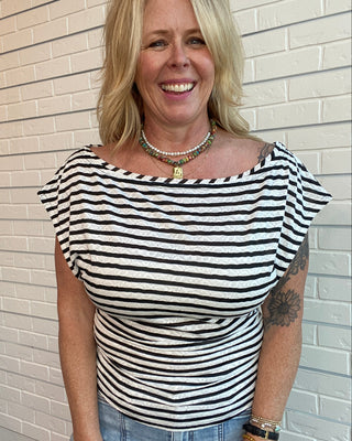 Woman wearing a black and white striped top standing against a brick wall.