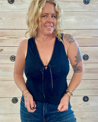 Woman wearing a black lace top and blue jeans against a wooden background