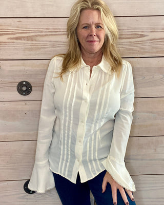 Woman wearing a white blouse and blue jeans against a wooden wall.