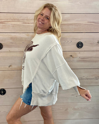 Woman wearing a white oversized shirt with a graphic design against a wooden wall.