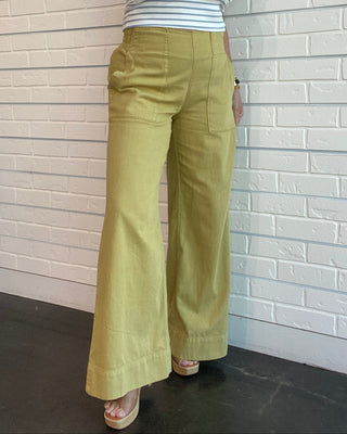 Person wearing green pants and a striped shirt against a light-colored wall.