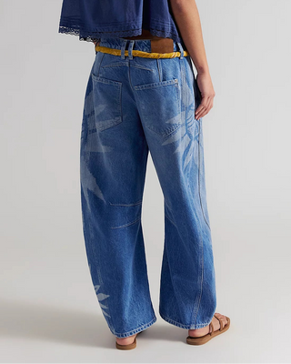Woman wearing a blue denim top and wide-leg jeans on a plain background