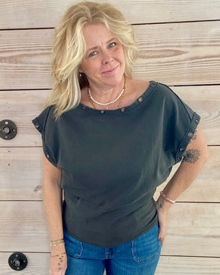 Woman wearing a dark grey top and blue jeans standing against a wooden background
