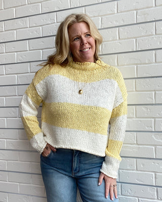 Woman wearing a yellow and white striped sweater against a light brick wall.