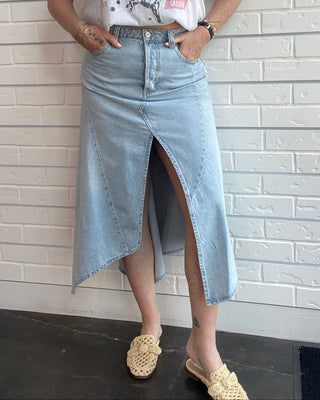 Woman wearing a graphic t-shirt and denim skirt against a white brick wall.